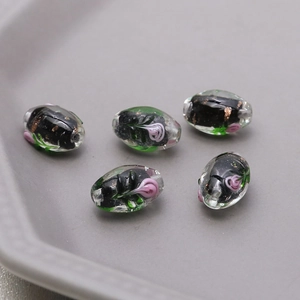 Close-up of five handmade lampwork glass oval beads with pink flowers and gold leaf details