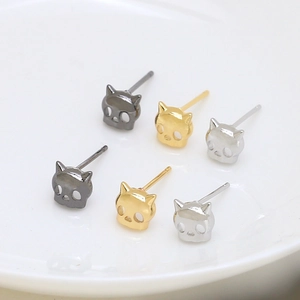 Detailed view of skull cat earrings in black, gold and silver finishes on a ceramic plate