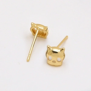 Detail of gold-plated cat-shaped skull studs with hollow eyes on white background