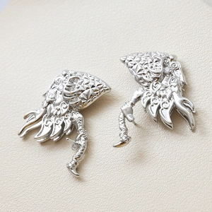 Close-up of silver-plated hollow carved flame earrings with zirconia on beige background