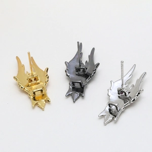 Three metal wing-shaped accessories in gold, silver, and black showing back details