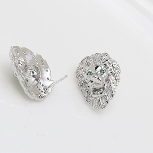 Detalle de pendientes de cabeza de león plateados con cristales blancos y ojos verdes