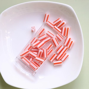 Close-up of orange and white striped tube beads in a clear storage box for DIY jewelry