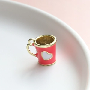 Vista macro di un mini ciondolo a tazza smaltato rosso con cuore su piatto bianco