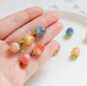 Handgehaltene Ansicht kleiner Erdbeeranhänger aus Harz in verschiedenen Farben für DIY-Schmuck