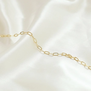 Dettaglio catena a maglie ovali placcata oro 14k su elegante tessuto di seta bianca