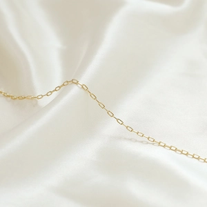 Vista macro di una sottile catena a maglie in oro 14k su sfondo di seta bianca