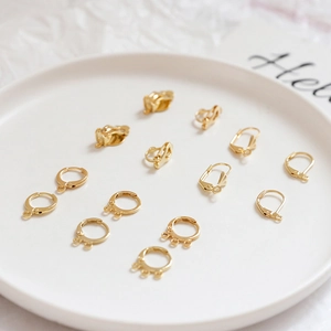 Macro detail of assorted 14k gold-plated earring findings on a white ceramic plate
