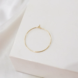 Close-up of minimalist 14k gold-filled hoop earring component on white geometric display
