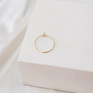 Macro shot of minimalist 14k gold-filled thin hoop earrings on a white stand