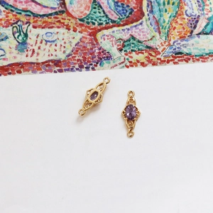Detail of 18k gold-plated double-hanging charms with oval purple stones and filigree
