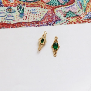 Detailed view of 18k gold plated connector links with oval green gems and vintage patterns