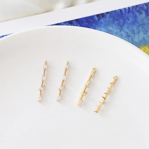 Detail of four gold-plated bar pendants with zircon settings in a white porcelain bowl