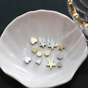 Macro shot of 14k gold and silver plated heart and star beads in a white shell dish
