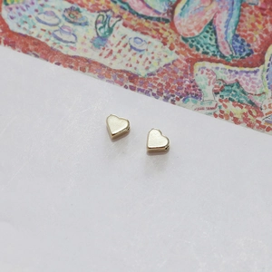 Detailed view of light gold heart-shaped metal beads with holes for DIY jewelry making