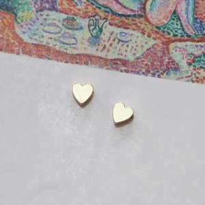 Close-up of polished 14k gold heart stud earrings on an artistic card background
