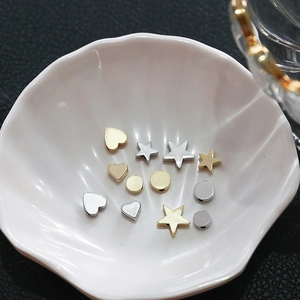 Star and heart shaped gold plated DIY jewelry beads displayed on a white shell plate