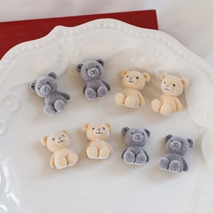 Detail of flocking teddy bear charms in beige and grey on a white ceramic plate