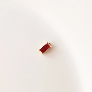 Detalle de colgante rectangular de circón rojo con base dorada para joyería artesanal