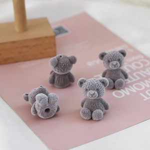 Detail of four grey flocked teddy bear charms with mounting holes for DIY crafts