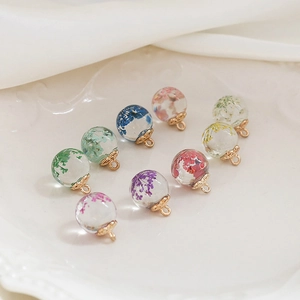 Macro detail of transparent glass ball charms with colorful dried flowers and gold caps