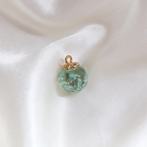 Close-up of glass ball charm with blue dried flowers and golden floral metal cap