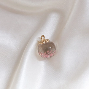 Close-up of a glass ball pendant with pink dried flowers and golden petal cap