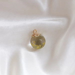 Detailed shot of transparent glass sphere pendant with yellow dried flowers and gold cap
