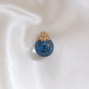 Detail of blue dried flowers inside a clear glass ball pendant with a gold metal cap