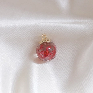 Macro detail of a glass globe pendant with red dried flowers and a textured gold cap