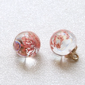 Macro shot of two transparent glass ball pendants featuring pink dried flowers and gold caps