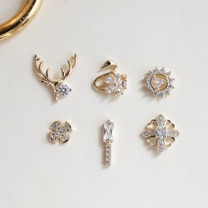 Macro detail of golden swan and floral nail charms with cubic zirconia inlay settings