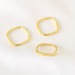 Detail of square gold plated rings with side inlaid zircon on white silk fabric