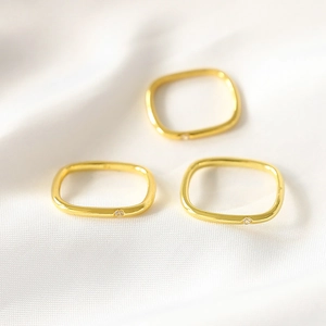 Close-up of three gold-plated square rings with small inset cubic zirconia on silk cloth