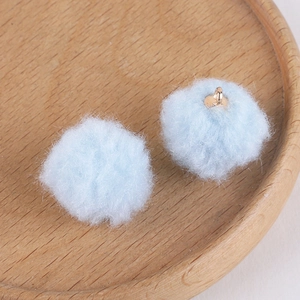 Detail of light blue fluffy pom-pom charms with gold metal loops on a wooden tray