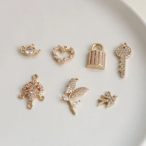 Détail de breloques dorées avec zircons incluant des motifs de cœur, serrure et oiseau