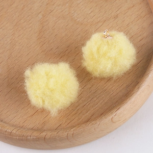 Close-up of yellow fluffy plush pom-pom charms with gold metal loops for DIY jewelry