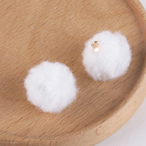 Close-up of two white fluffy plush pom-pom charms with gold metal loops on wood tray