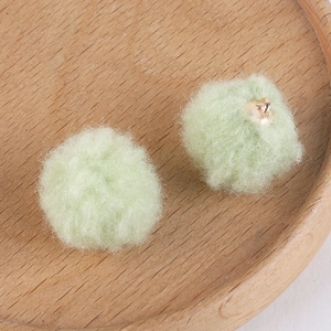 Detail of soft light green plush pom-pom charms with gold metal rings for DIY jewelry