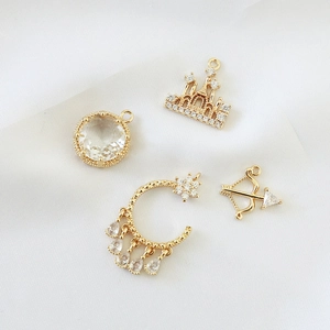 Macro detail of gold-plated castle and arrow charms with zircons on white silk