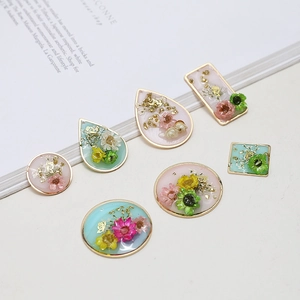 Macro detail of geometric resin charms featuring dried flowers and gold foil accents