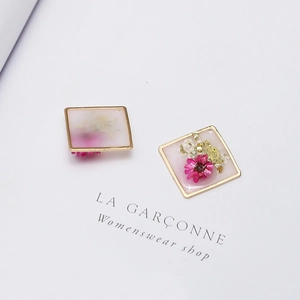 Detailed macro view of square gold-plated resin pendants with embedded dried flowers