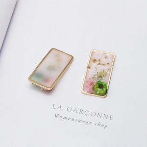 Detail of rectangular resin charms with pink dried flowers and gold foil in metal frames