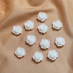 Detail van tien witte iriserende harsroosbedeltjes op gouden satijnen stof voor sieraden