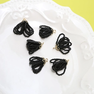 Macro detail of six black beaded fringe pendants with embossed gold metal flower caps
