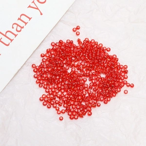 Macro shot of loose 2mm transparent red glass seed beads on a white textured background