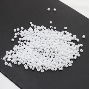 Macro view of 2mm white porcelain seed beads stacked on a black surface for DIY jewelry