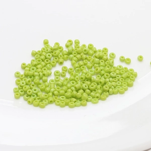 Detailed view of 2mm grass green seed beads in a white bowl for DIY jewelry making