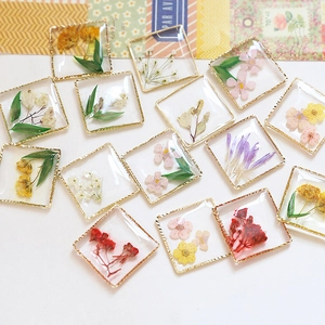 Dettaglio macro di ciondoli quadrati in resina con fiori secchi e cornice in metallo oro