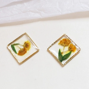 Dettaglio macro di orecchini quadrati dorati con fiori secchi gialli in resina
